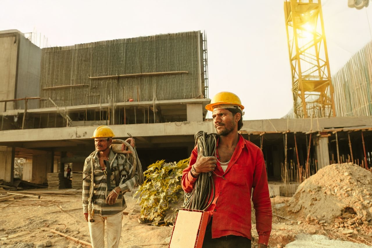 Free Two construction workers wearing helmets at a site in India with a crane and building. Stock Photo