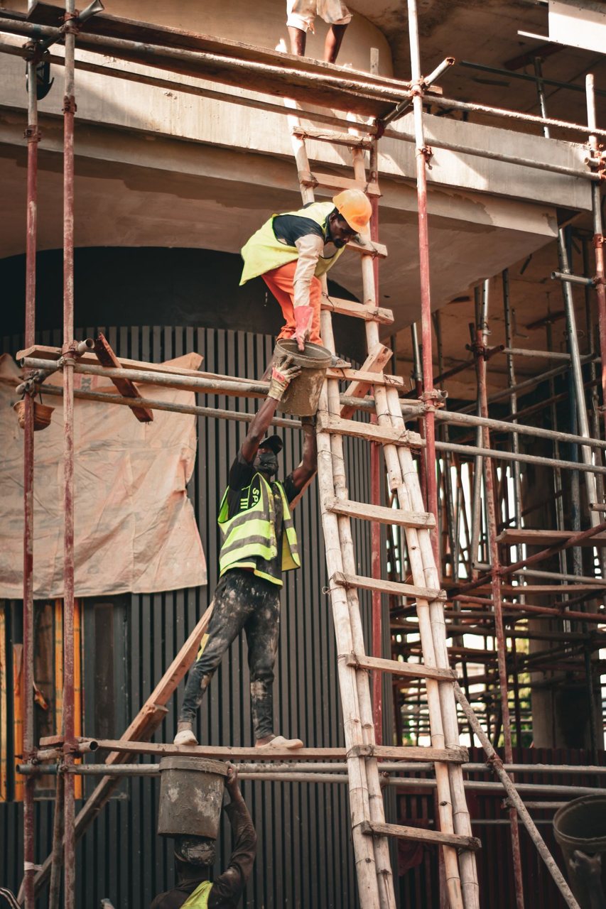 Free Two construction workers in safety gear collaborate on scaffolding at a building site. Stock Photo