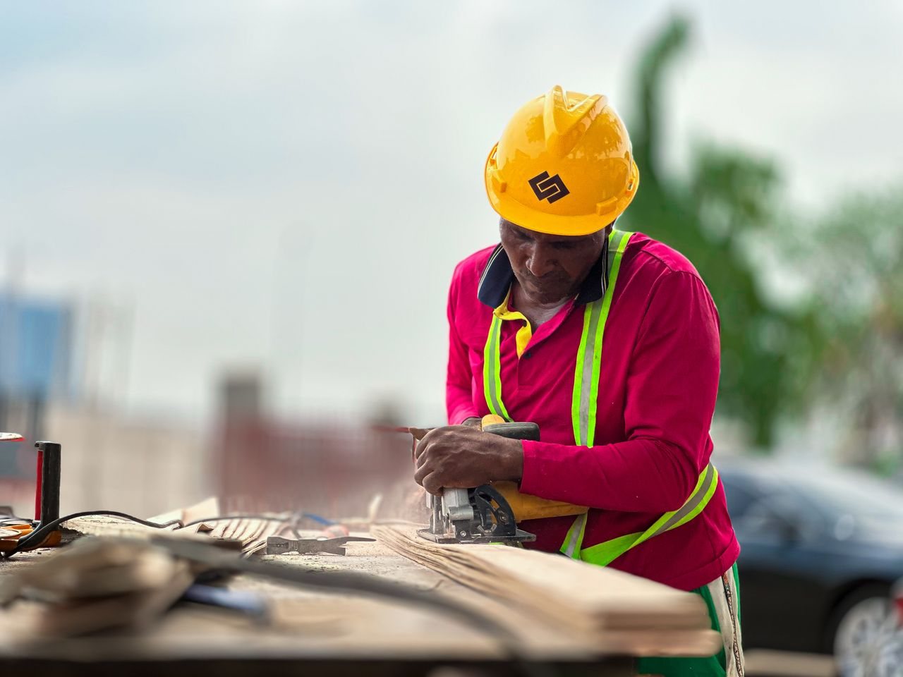 Free Construction worker cutting wood with a power tool outdoors, wearing safety gear. Stock Photo